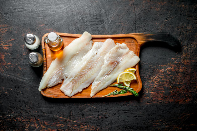 罗非鱼把鱼片放在砧板上 用柠檬片 油和香料放在深色的乡村餐桌上去骨美食油