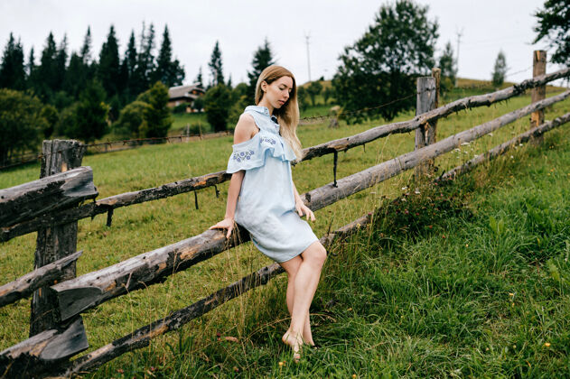 服饰年轻漂亮的金发碧眼的女孩 穿着蓝色的裙子 在乡村的篱笆边摆姿势女孩篱笆人