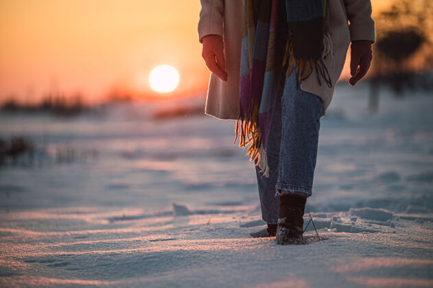 雪日落时分 在冬天的乡下 在新鲜的白雪上 收割着一个穿着暖和的衣服和靴子 面目全非的女人冒险模糊鞋履