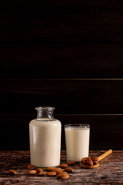 素食主义者杏仁牛奶装在一个瓶子和一个玻璃杯里 在深色复古木背景上 有复制空间玻璃杏仁杏仁奶