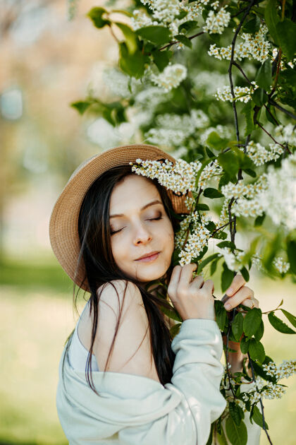 气味年轻漂亮的女人靠近鸟樱花樱花盛开的小鸟和戴着帽子的快乐女人过敏夏天时尚