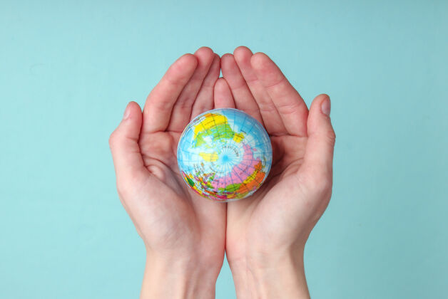 大陆地球在一个女性手掌上蓝色墙壁地球护理概念地球全球手指