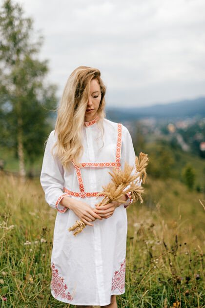 金发年轻迷人的金发女孩 穿着白色连衣裙 戴着小穗花束在风景如画的乡村风景中摆姿势乡村自然女孩