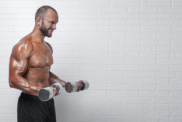 运动员健美运动员在砖墙上用哑铃练习二头肌体格运动腹部