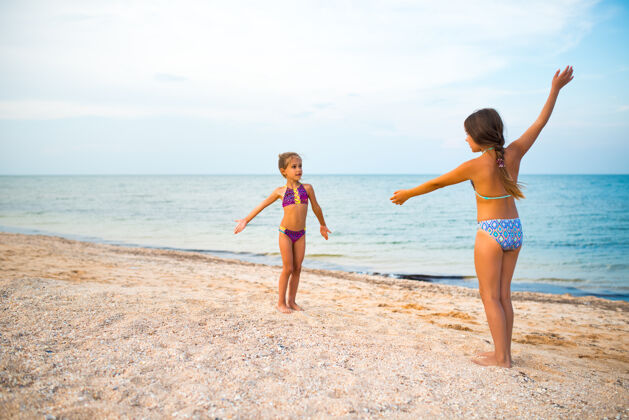 海洋积极的小女孩姐妹们在阳光明媚温暖的夏日 在沙滩上积极地玩游戏杂技演员贝壳站立