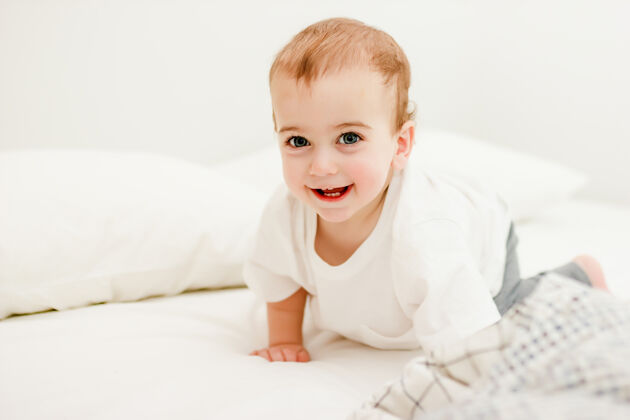 小在家的床上爬着的穿着白色T恤的婴儿护理微笑小