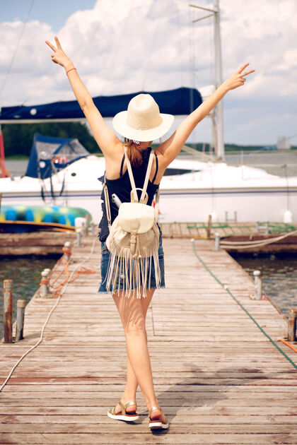 码头夏天戴草帽的女人仰面站在码头上 举起双臂 伸出两个手指夏天巡航人
