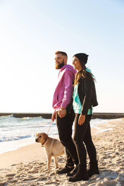 狗可爱的年轻夫妇和他们的狗在海滩散步男人团结肖像