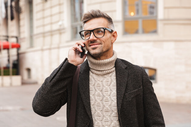连接穿着外套的帅哥走在户外 讲着手机年轻通话说话