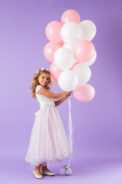 孩子一个穿着公主裙的漂亮小女孩孤零零地站在紫罗兰色的墙上 手里拿着一堆气球吸引力小空气