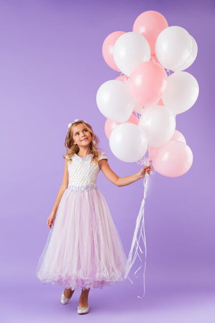 孩子一个穿着公主裙的漂亮小女孩孤零零地站在紫罗兰色的墙上 手里拿着一堆气球公主白种人爱
