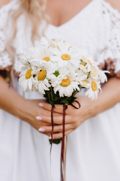 花瓣一束雏菊在新娘的手中 背景是一件白色的连衣裙女人花花朵