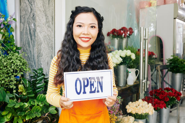 消费主义美丽的越南年轻女子站在花店开放标志的画像销售职业玫瑰服务