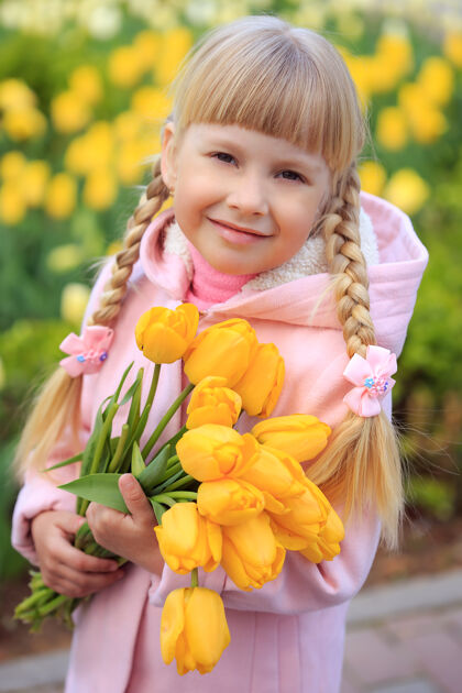 女孩可爱的小女孩手持一束黄色郁金香 背景是美丽的花朵一个穿粉红色外套的女孩爱庆祝年轻