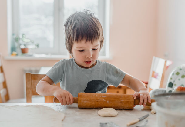 童年厨房里一个小男孩用擀面杖准备饼干的画像小厨房助手