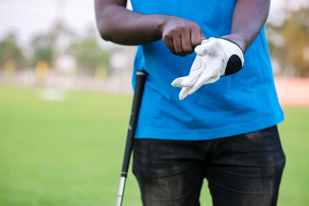 比赛手戴高尔夫手套在高尔夫球场的球杆上背景活动球道