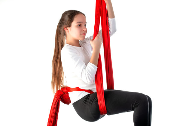 年轻人一个穿着白色毛衣和黑色紧身裤的可爱少女正在用一条红色的飘带在白色的裙子上做运动杂技悬挂平衡活跃