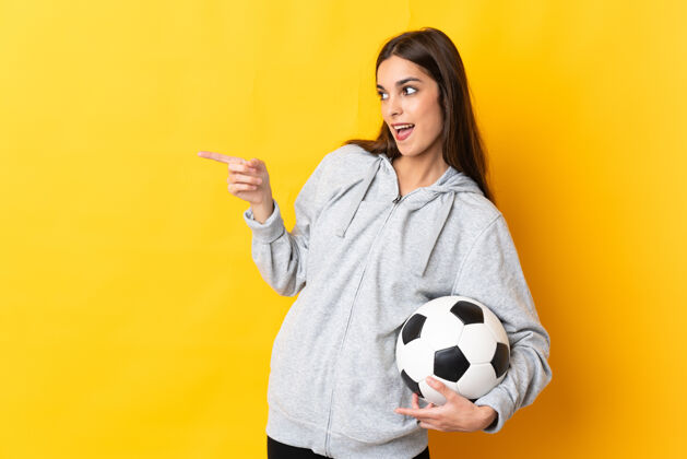 自信一个年轻的足球运动员 一个被隔离在黄色背景下的女人 手指着侧面 展示着一个产品表情看快乐