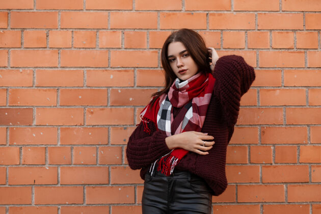 裤子身穿紫红色毛衣和黑色皮裤的年轻女子站在城市的砖墙附近紧身裤衣服户外