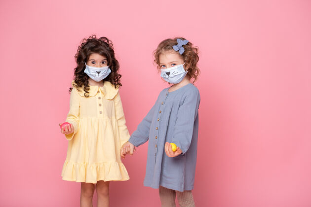 检疫两个戴着保护面具的女孩手里拿着粉色彩蛋女孩孩子朋友