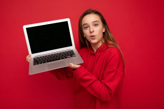 深色美丽的年轻女孩拿着笔记本电脑看着彩色背景下的相机哇电脑上网本