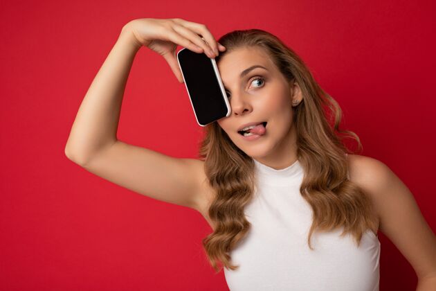 通信快乐性感迷人的年轻金发女性穿着白色t恤隔离在红色背景上设备电话欢呼