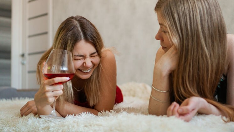 浪漫两个朋友躺在沙发上聊天漂亮金发女郎手里拿着一杯红酒酒店微笑卧室