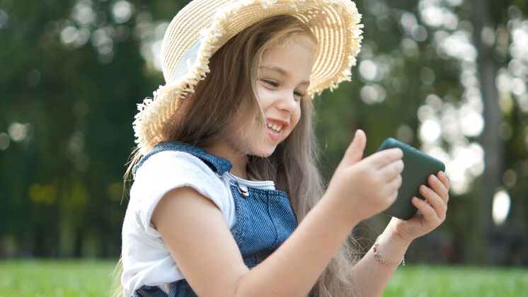 乐趣快乐微笑的小女孩在夏天的户外看手机数字看小