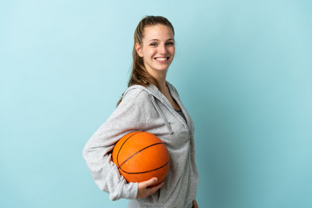 运动装年轻的白人女子在蓝色背景下打篮球积极年轻运动员