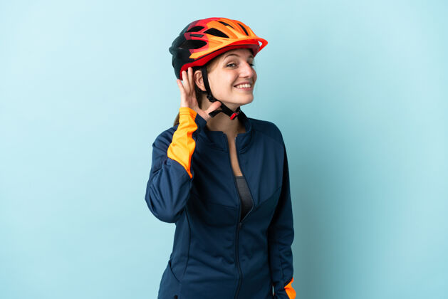 运动一个骑自行车的年轻女子被隔离在蓝色背景下 用手捂着耳朵听东西听骑车人表情