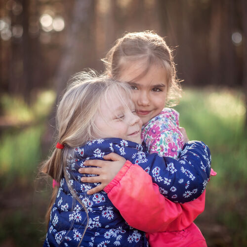 高兴可爱的女孩在秋天的森林里散步 用爱和温柔拥抱着她的小妹妹 全国拥抱和友谊日 休闲的生活方式 户外享受候选人秋天