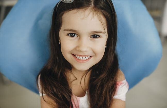 人一个可爱的小女孩坐在儿科口腔科看着相机笑着牙齿手术前的画像诊所初级牙科
