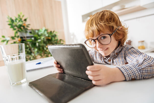 电脑你在看什么在高飞一个可爱的红头发小孩早上坐在桌子旁 戴着眼镜 在他的小玩意儿上读着什么孩子永远阳光