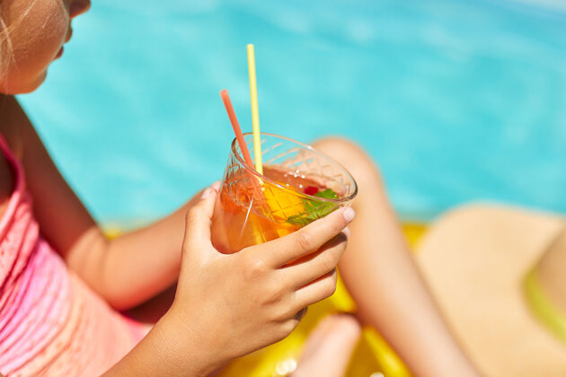 人小女孩在游泳池里放松 享受日光浴 在家庭度假时在水里的黄色充气床垫上喝果汁可爱房子晒黑