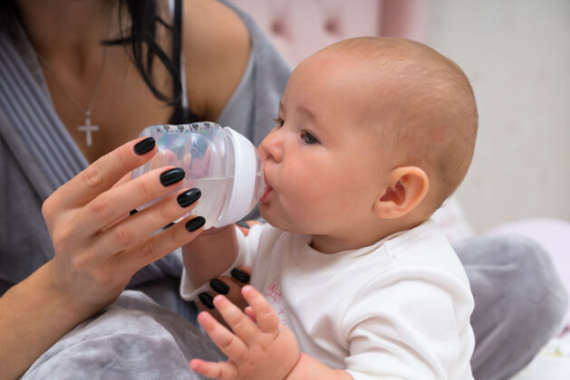 关系妈妈用奶瓶喂她可爱的小宝宝在近距离看宝宝喝酒父母肖像托儿所