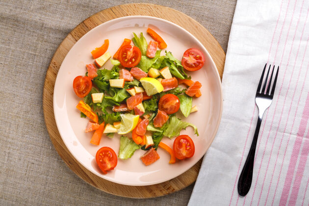 开胃菜在一个灰色表面的盘子里放一份三文鱼和樱桃西红柿沙拉 放在叉子和餐巾旁边的木架上沙拉鳄梨菠菜