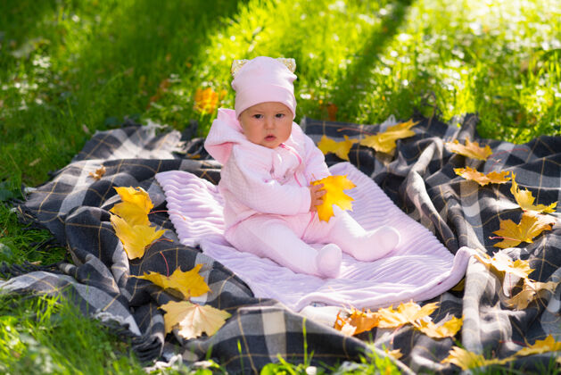 秋天小女婴坐在户外的地毯上 绿色的草地上散落着五颜六色的黄色秋叶人小独自