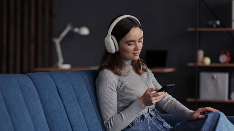 房子戴着耳机微笑的年轻女孩的肖像 在移动应用程序中选择喜爱的音乐曲目女孩耳机应用