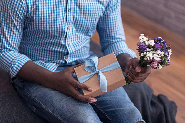 微笑出席你靠近点高兴的男人拿着鲜花和礼物 准备给他女朋友一个惊喜家庭室内伴侣