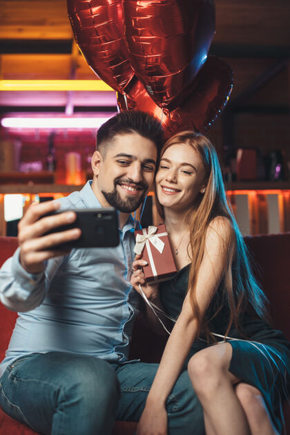 带一对高加索夫妇在情人节手持红气球 一边用手机和微笑自拍快乐雀斑情人节