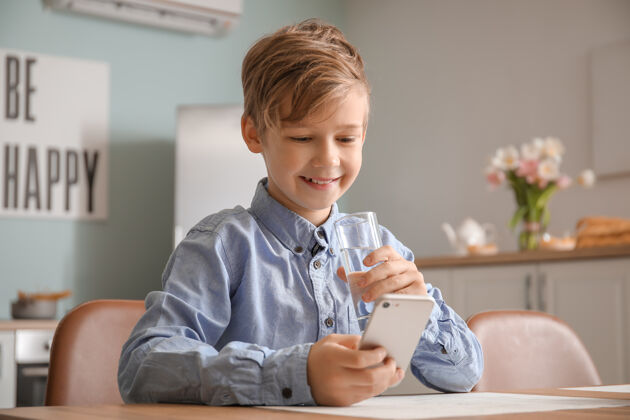 肖像可爱的小男孩拿着手机在厨房喝水能量纯净电话