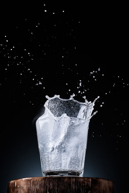 泡沫纯矿泉水在一个玻璃杯里 冰掉进水里玻璃飞溅水在玻璃上升起 深色的墙壁上有文字的地方 有选择性聚焦关闭-向上 垂直框架口渴器皿健康