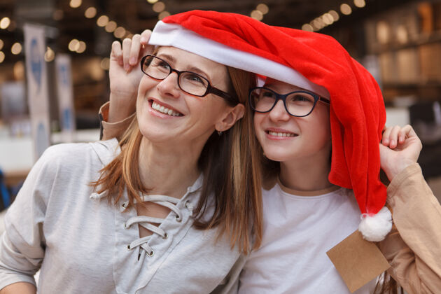 家具开朗成熟的女人和她十几岁的女儿笑着 戴着圣诞老人的帽子年轻室内女学生