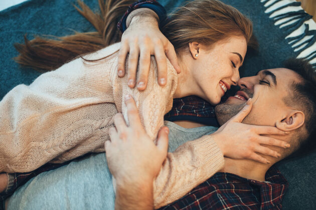 情人上图：一对可爱的年轻夫妇面面相觑地笑着倚在床上 女孩抚摸着她的男朋友的脸床成人男人