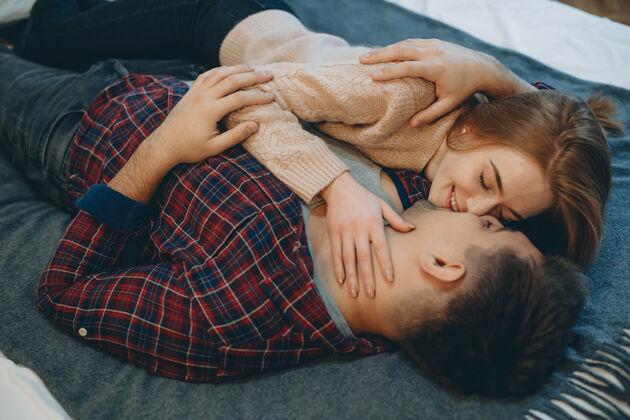 性感俯视图：一对迷人的年轻夫妇在床上面对面地拥抱 在接吻前笑着 而女孩在抚摸她的男朋友的脸室内浪漫吻