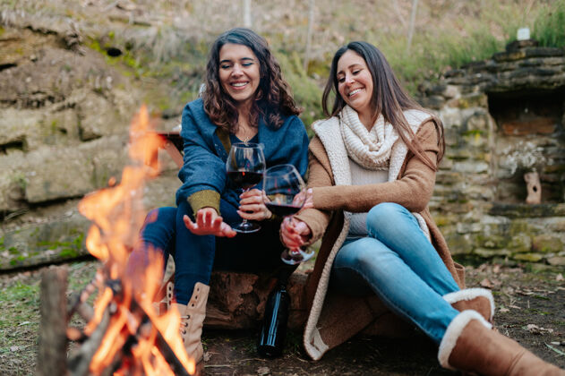 欢呼年轻快乐的女人喝着一杯红葡萄酒葡萄酒女性温暖的天气篝火户外活动概念红酒酒喝酒