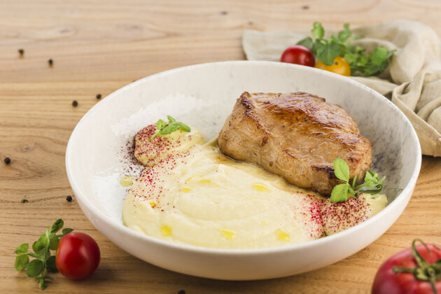 切猪肉牛排和土豆泥放在一个盘子里 放在一个浅色的木头表面上菜盘子饭
