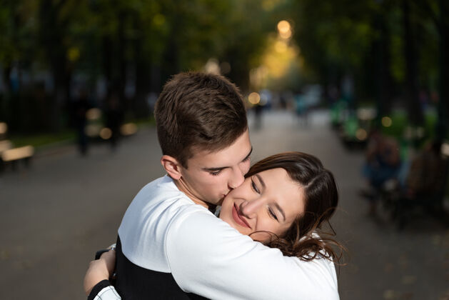 黑发北京一对美丽的年轻夫妇的画像帕克盖伊轻轻地吻了女孩的脸颊户外公园男孩