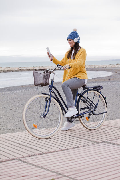 自行车美丽活泼的熟女骑着自行车在路边海快乐微笑的中年女子戴着耳机听音乐 复制空间户外娱乐海洋
