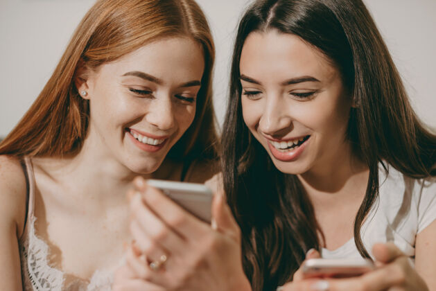 社交媒体两个漂亮的小妹妹看着智能手机屏幕笑的特写照片电话沙发朋友